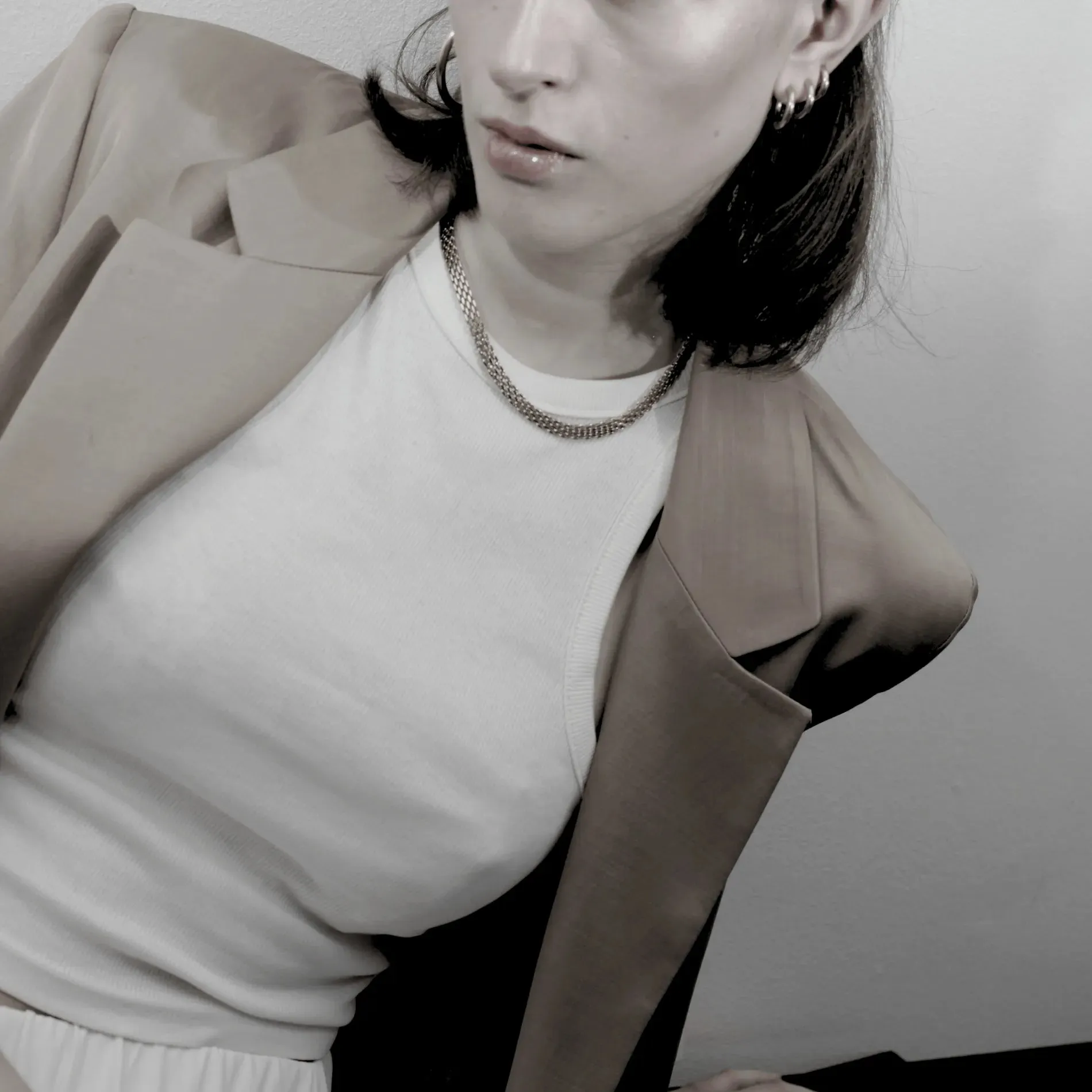 Kvinna i beige kavaj och vit topp med kedjehalsband i minimalistisk stil.